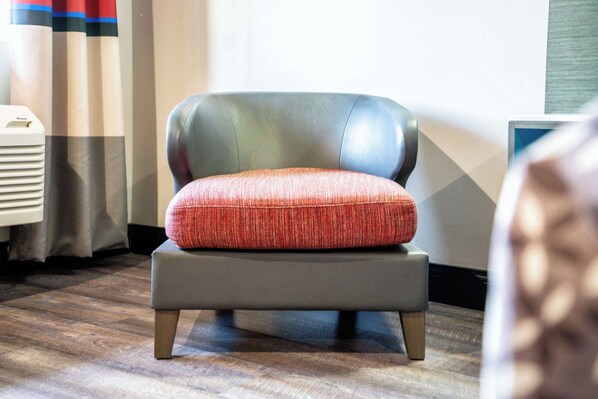 A modern office chair with a red cushion, positioned on a wooden floor.