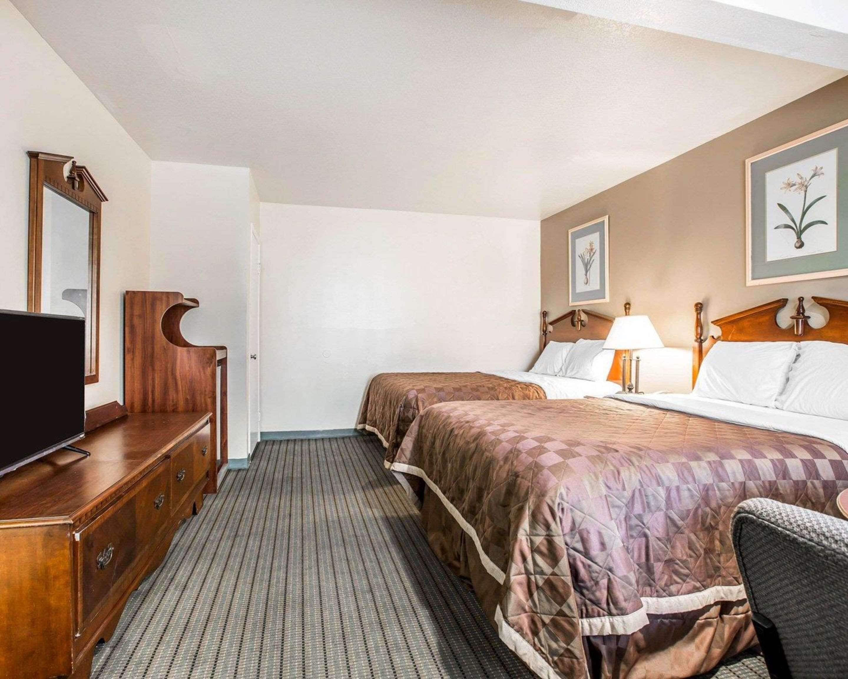 A hotel room with two beds, a TV, a wooden dresser, and a framed picture on the wall.