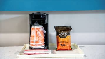 Uma cafeteira, uma cápsula de café e um pequeno sachê de leite para café em uma bandeja.