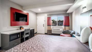 Quarto de hotel com cama, escrivaninha, televisão na parede, janela com cortinas e aquecedor.