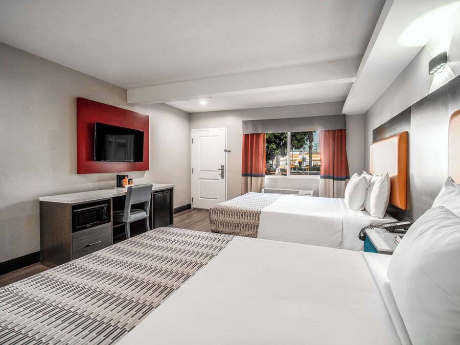 Quarto de hotel com duas camas, uma escrivaninha, televisão e janela com cortinas.