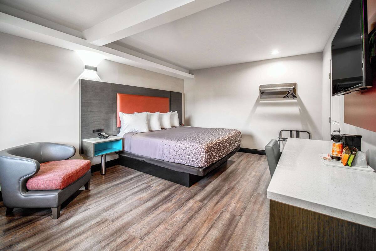 A modern hotel room with a bed, a desk, a chair, and a TV.