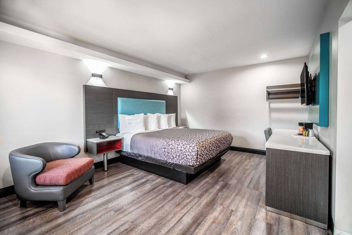 A modern hotel room with a bed, a chair, a desk, and a TV mounted on the wall.