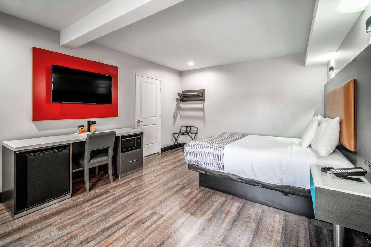 A modern hotel room with a bed, desk, and TV.