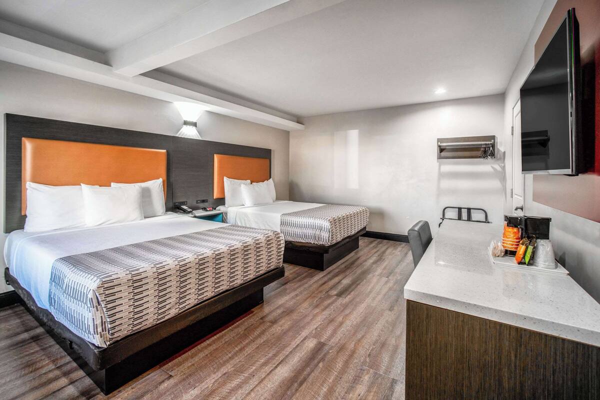 A hotel room with two beds, a desk, and a TV.