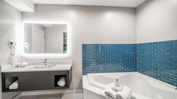 A modern bathroom with a white vanity, a large mirror, a blue-tiled shower area, and a white bathtub.