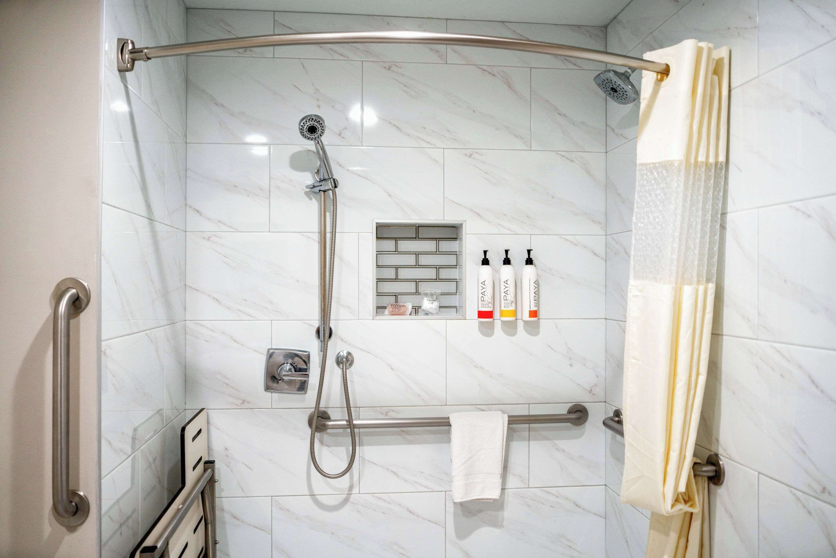 Un baño moderno con ducha, barras de apoyo, toallero y artículos de aseo.