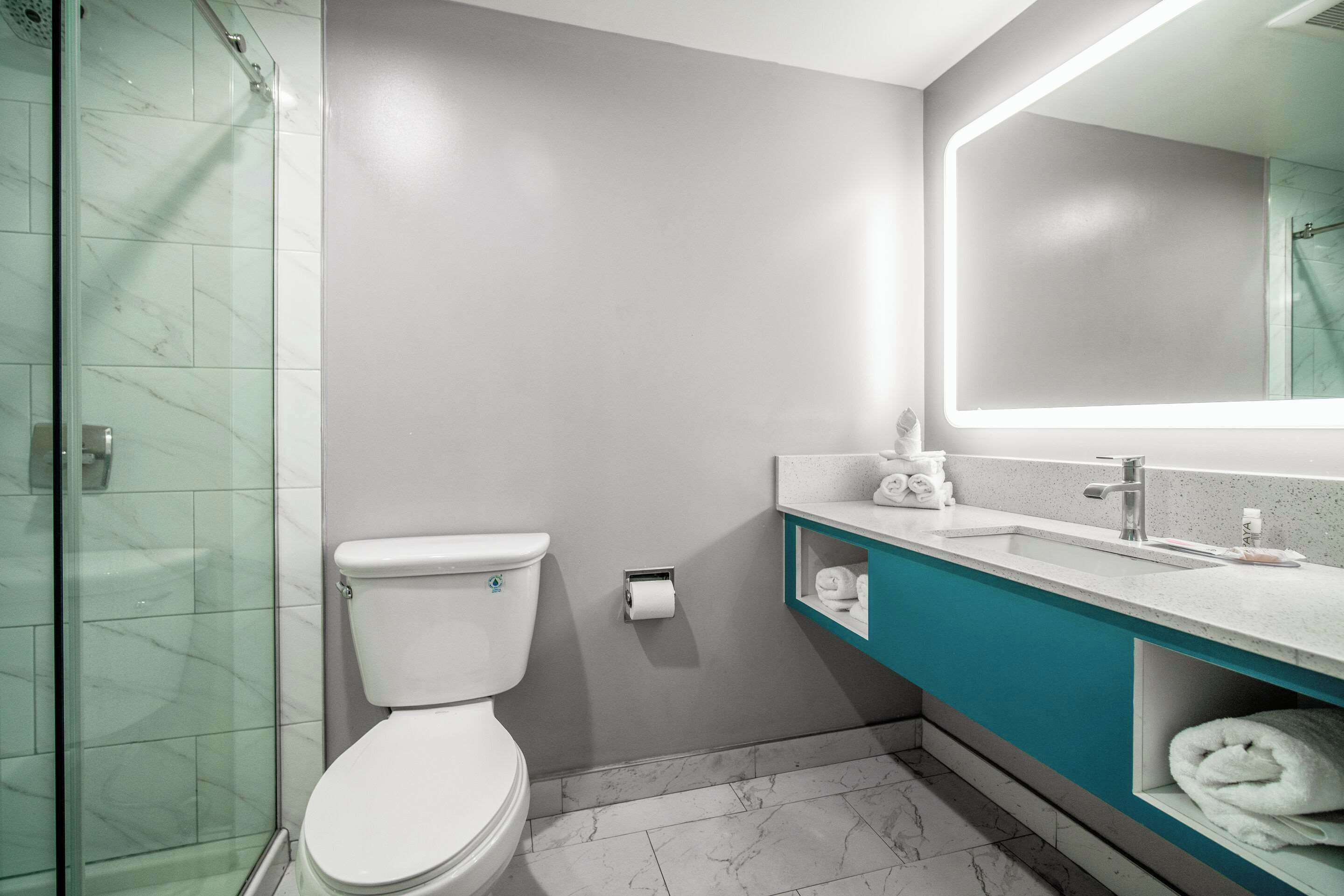 A modern bathroom with a glass shower enclosure, a white toilet, a sink with a mirror, and a teal vanity.