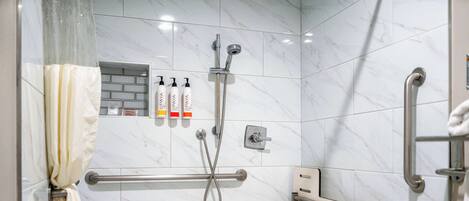 Ein Badezimmer mit weißen Marmorfliesen, einer Dusche inklusive Handbrause, einer Haltestange und einem Handtuchhalter.