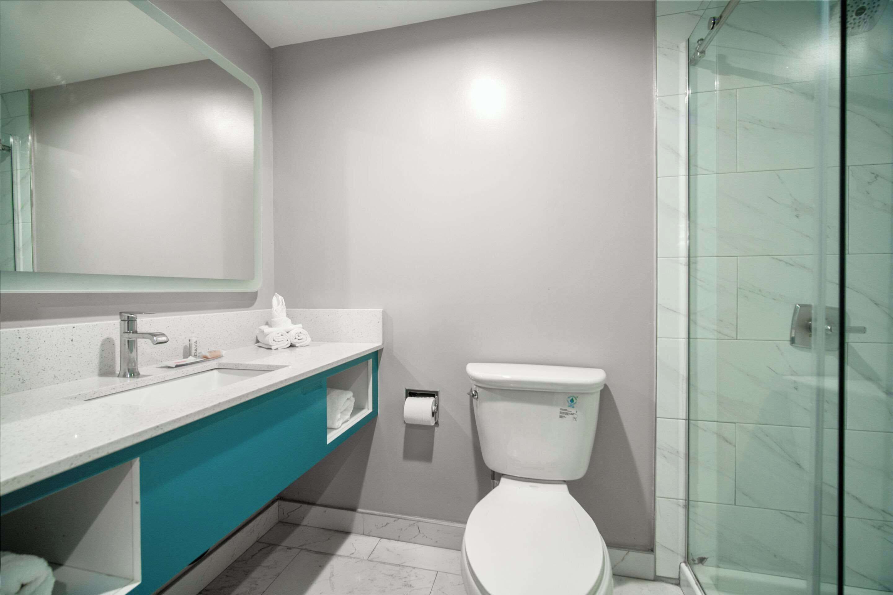 A modern bathroom with a glass shower enclosure, a white toilet, and a teal vanity with a mirror.