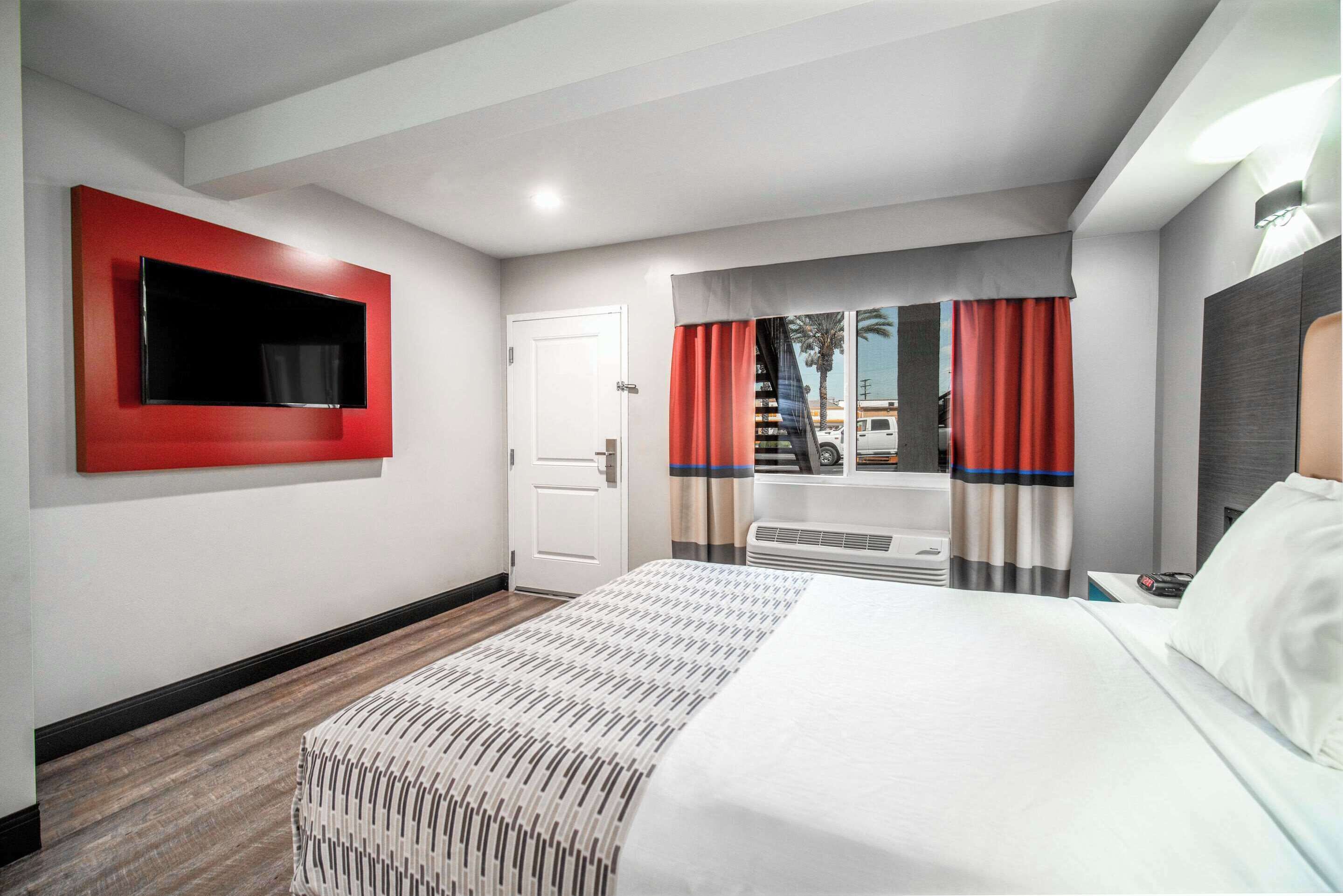 A hotel room with a large bed, a flat-screen TV mounted on the wall, a window with curtains, and a door.