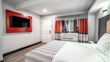A hotel room with a large bed, a flat-screen TV mounted on the wall, a window with curtains, and a door.