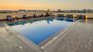 A rooftop pool with lounge chairs and tables, surrounded by a cityscape view. - Goldfinch Hotel Mumbai (Mumbai)