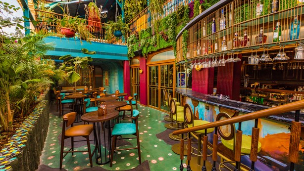 An indoor bar with multiple seating areas, a bar counter, and a variety of plants and greenery. - Goldfinch Hotel Mumbai (Mumbai)
