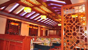 A restaurant with wooden beams and patterned ceiling panels, booths with floral upholstery, and hanging yellow pendant lights. - Supreme Hotel (Pune)