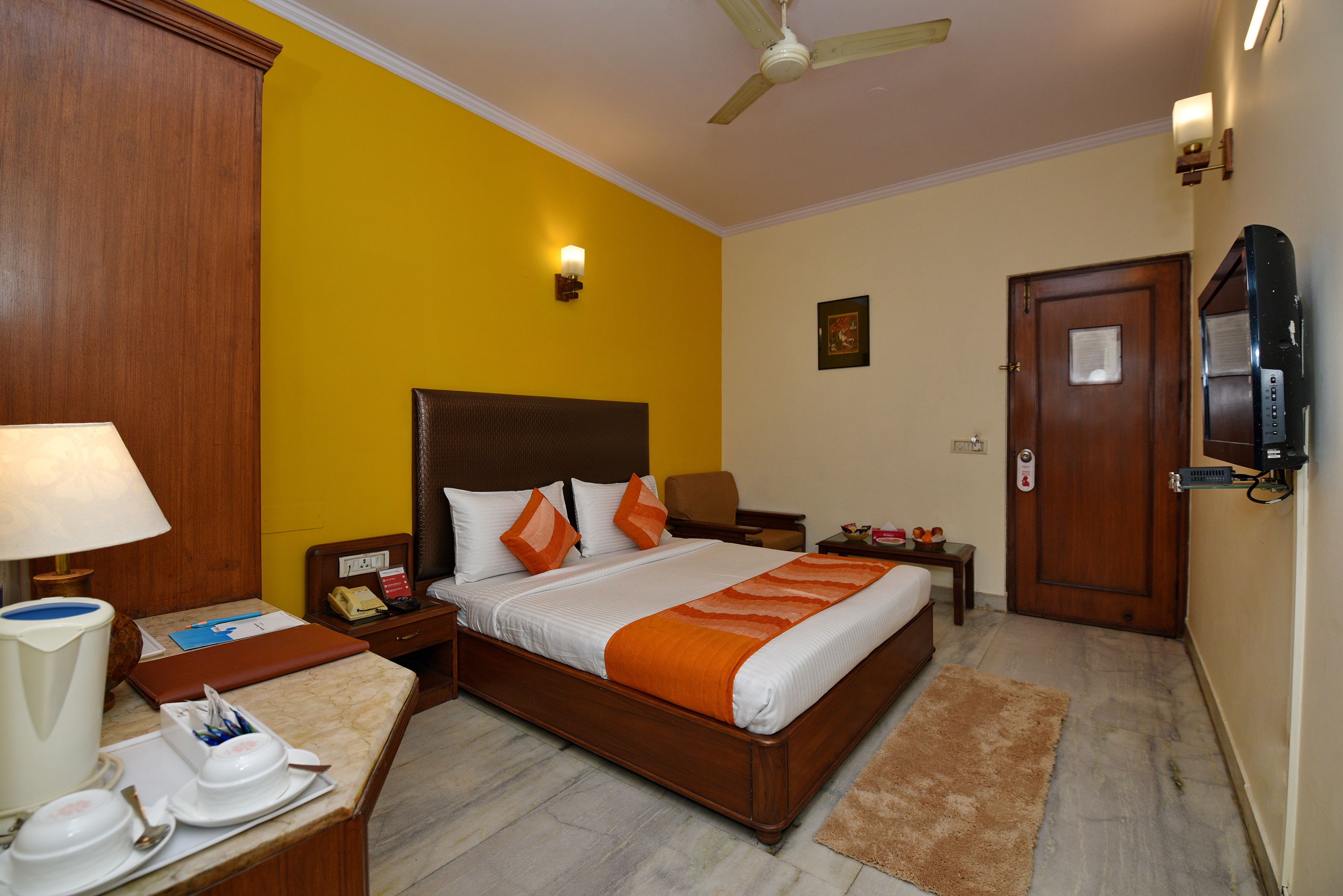 A hotel room with a bed, bedside tables, a desk with a lamp, a chair, a television, and a door.
