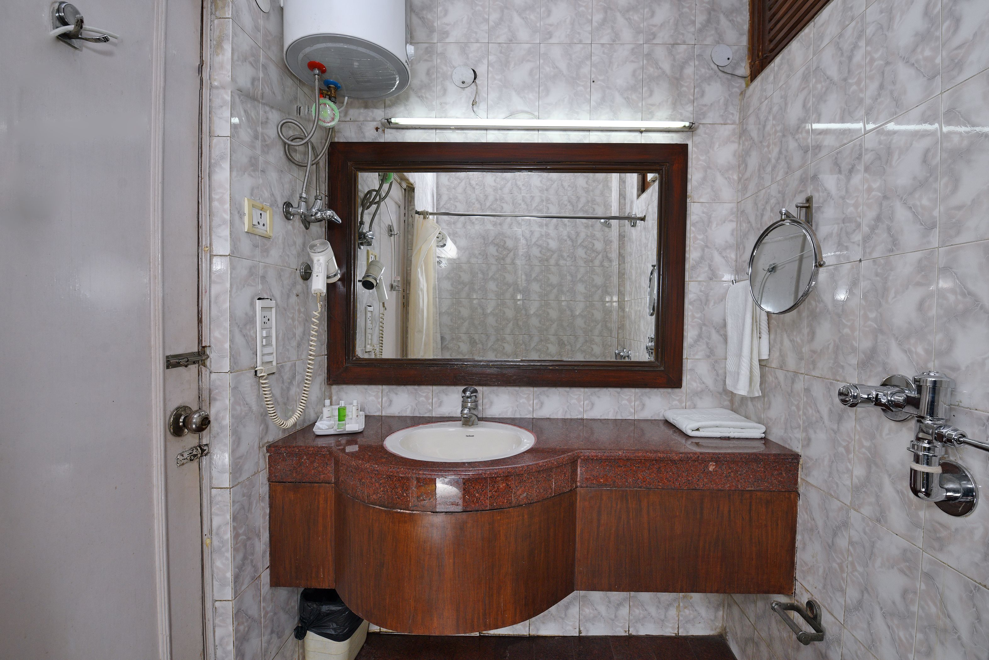 A bathroom with a marble-tiled wall, a wooden vanity with a sink, a mirror, and a towel rack.