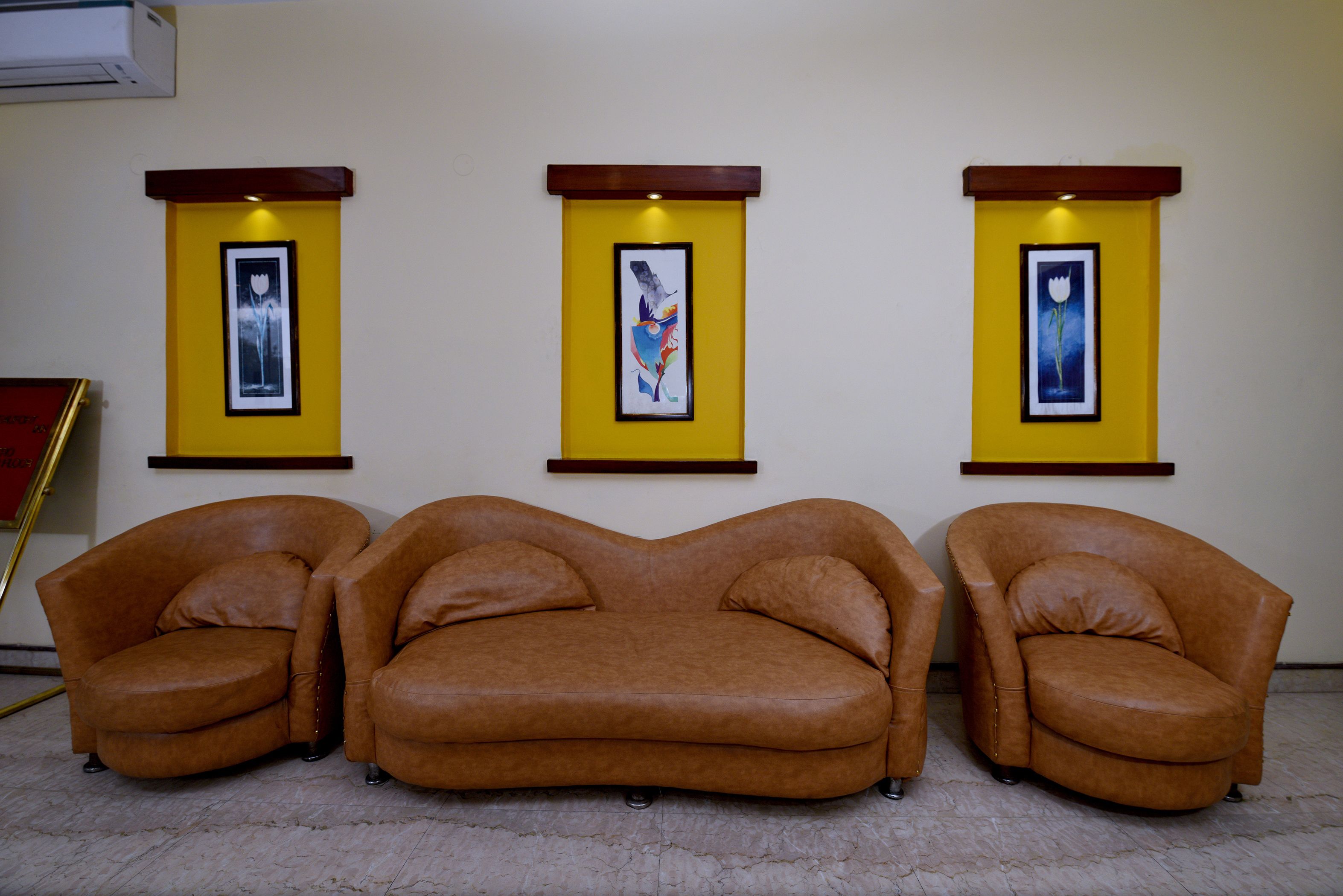 Una habitación con tres sofás de cuero marrón colocados en fila frente a una pared amarilla, con tres cuadros enmarcados encima.