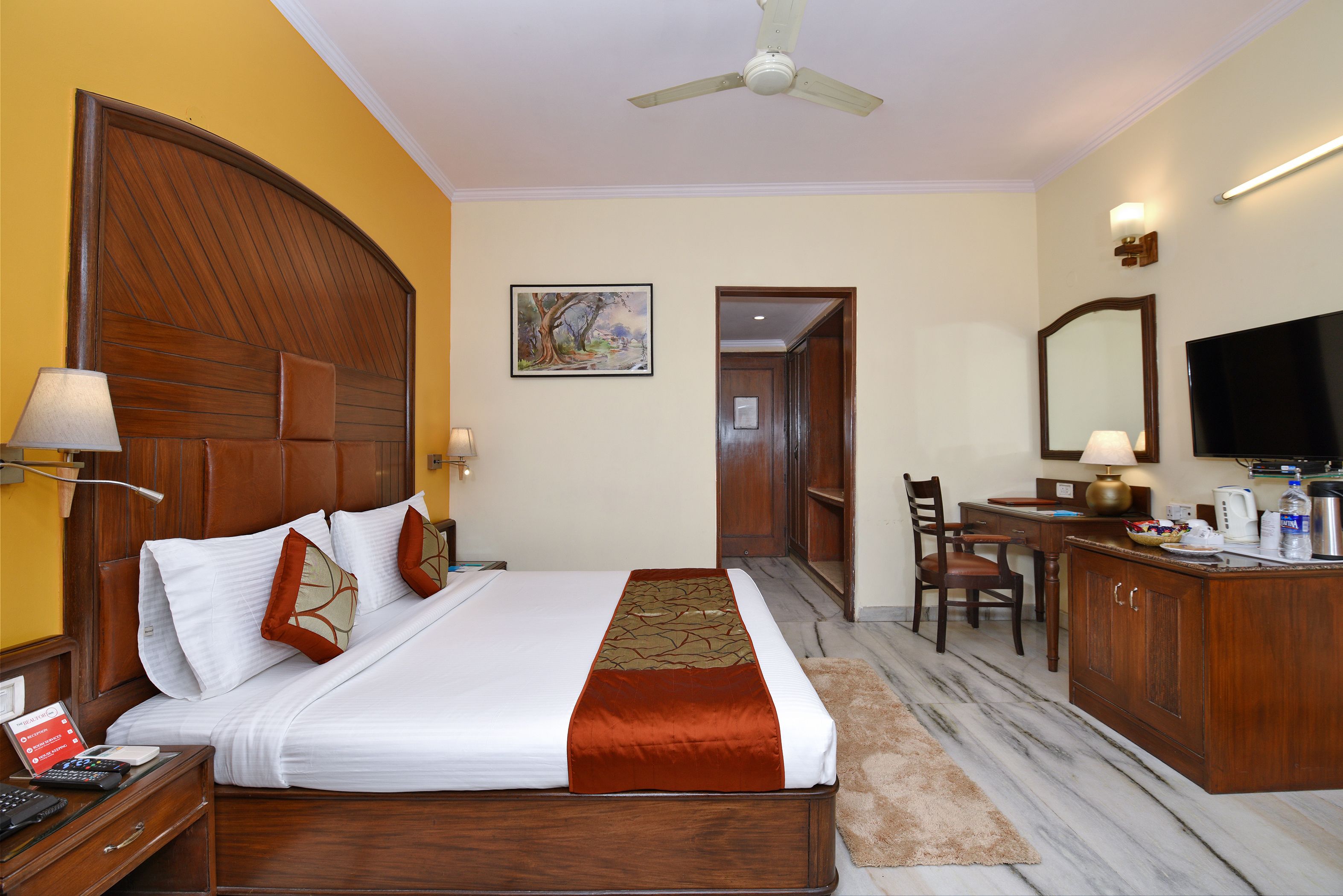 A hotel room with a large bed, wooden headboard, a desk with a chair, a television, and a bathroom door.