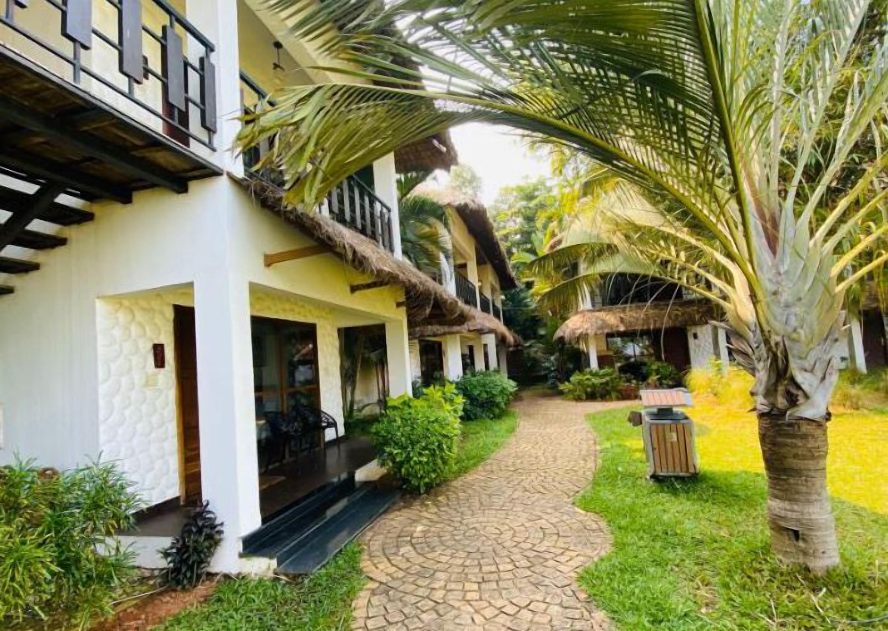 A pathway leading to a building with a thatched roof and a covered outdoor seating area.