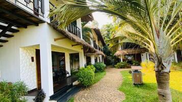 A pathway leading to a building with a thatched roof and a covered outdoor seating area.
