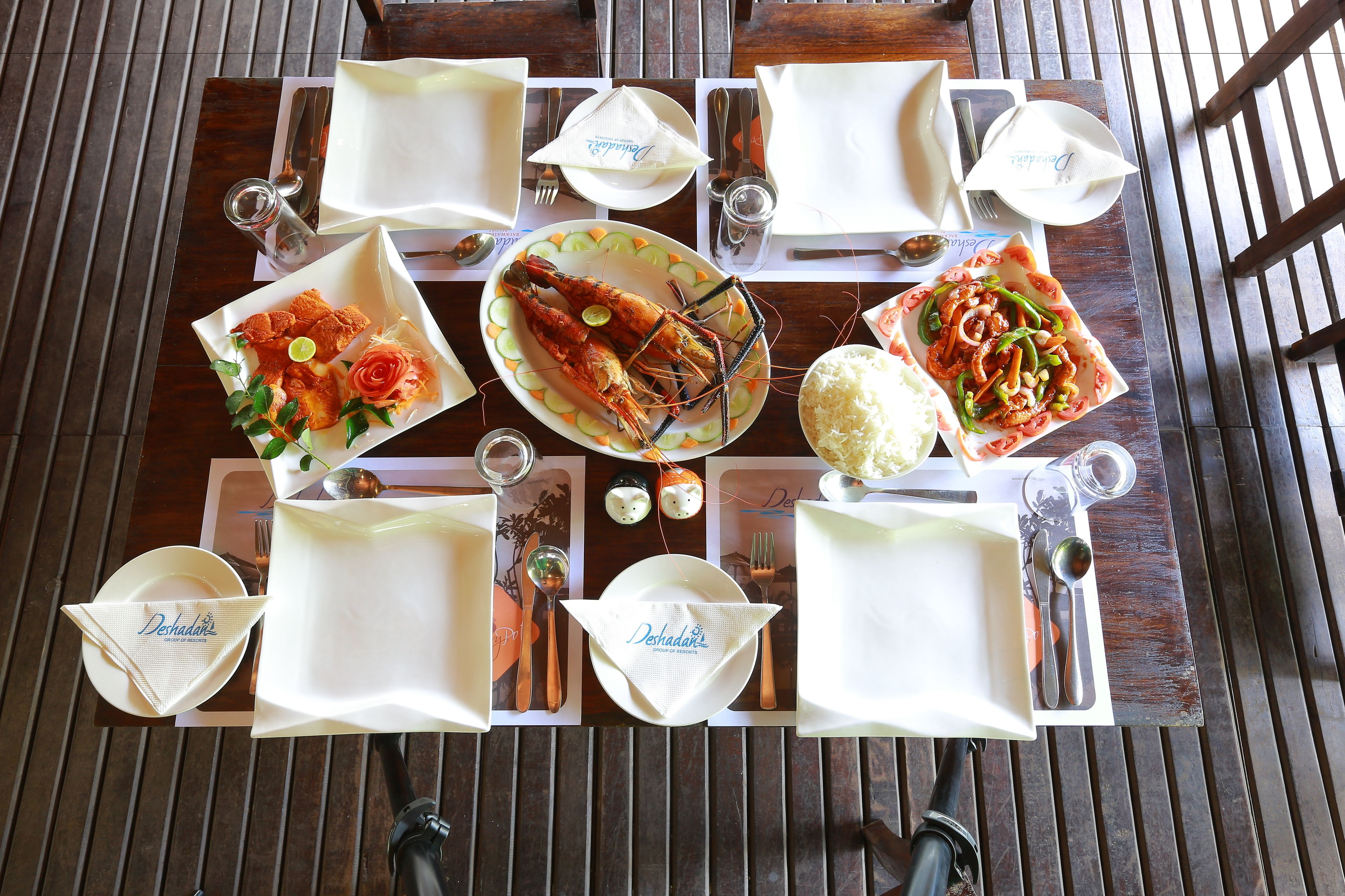 Mesa de jantar posta com pratos, talheres e diversos pratos, incluindo mariscos e arroz.