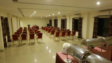 A conference room with rows of red chairs, a buffet area with a grill, and air conditioning units on the walls.