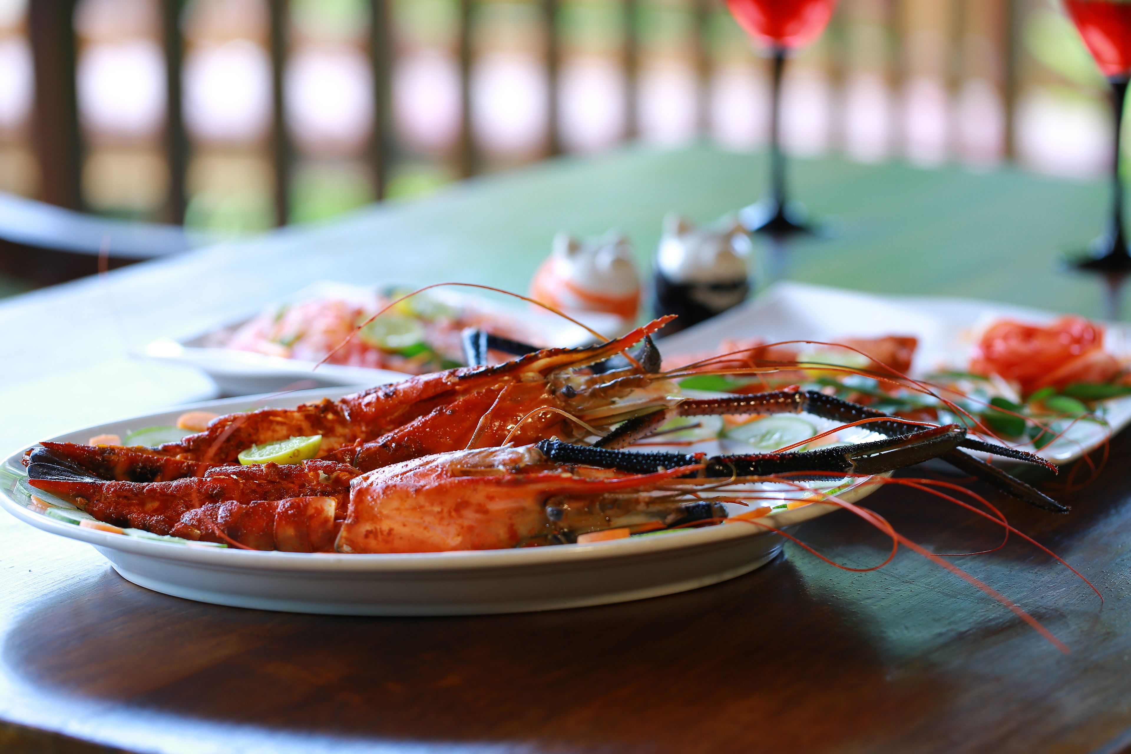 A seafood dish with a lobster on a plate, accompanied by a small bowl of sauce and a glass of red drink on a table.