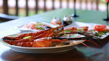 A seafood dish with a lobster on a plate, accompanied by a small bowl of sauce and a glass of red drink on a table.