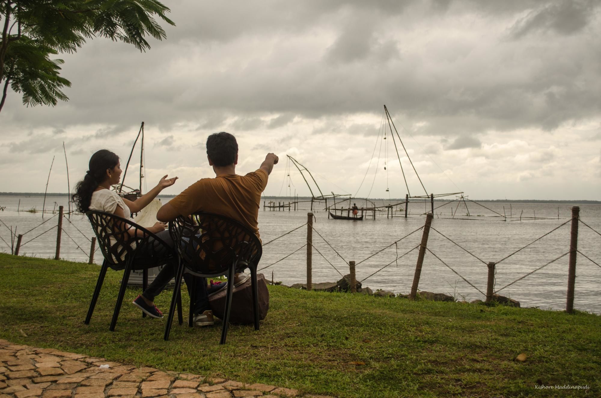 Two people sitting on chairs facing a body of water with fishing nets.