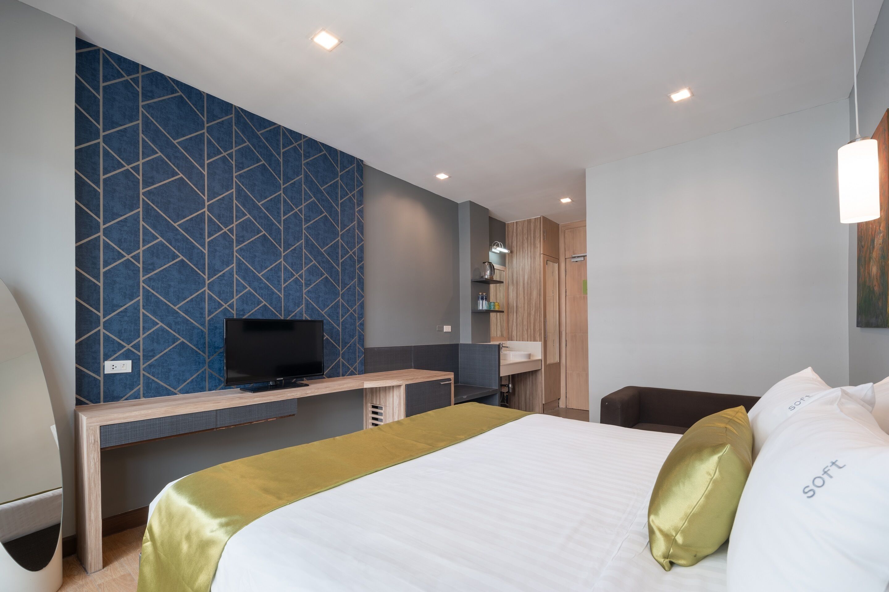 Quarto de hotel com cama, escrivaninha, televisão, guarda-roupa e banheiro.