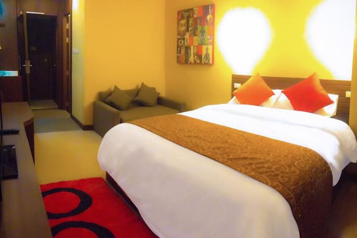 A hotel room with a bed, a sofa, a painting on the wall, and a red rug.