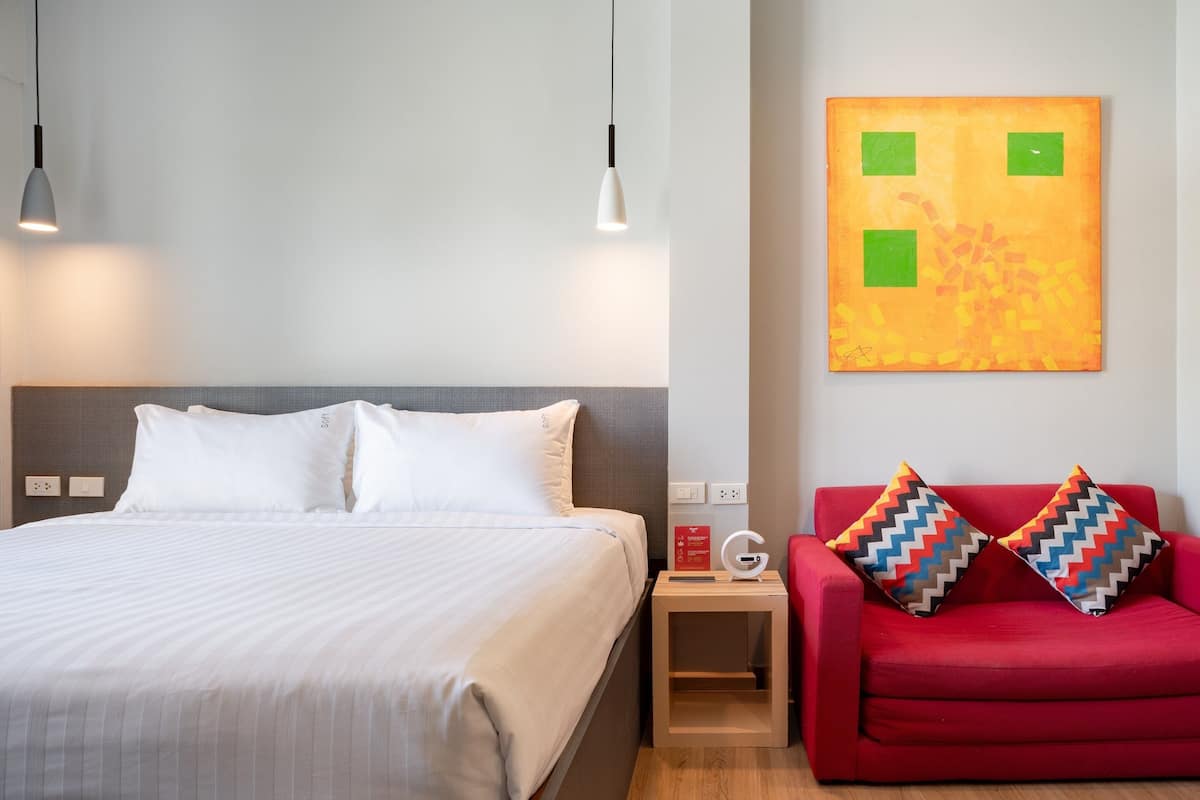 Habitación de hotel con cama, mesita de noche, sofá rojo y una obra de arte en la pared.