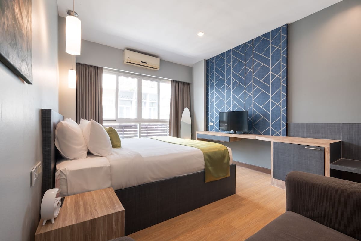 Una habitación de hotel moderna con cama, mesita de noche, televisión y escritorio con silla.