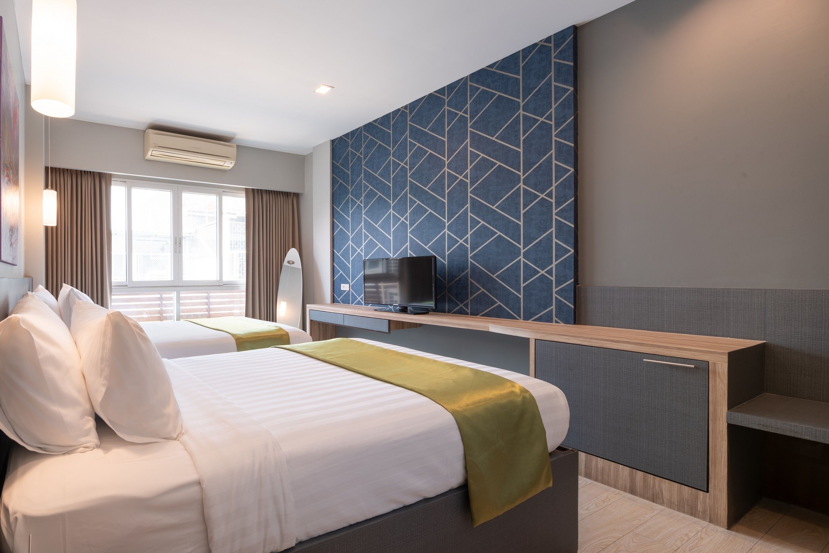 A hotel room with two beds, a TV, a desk, and a large window with curtains.