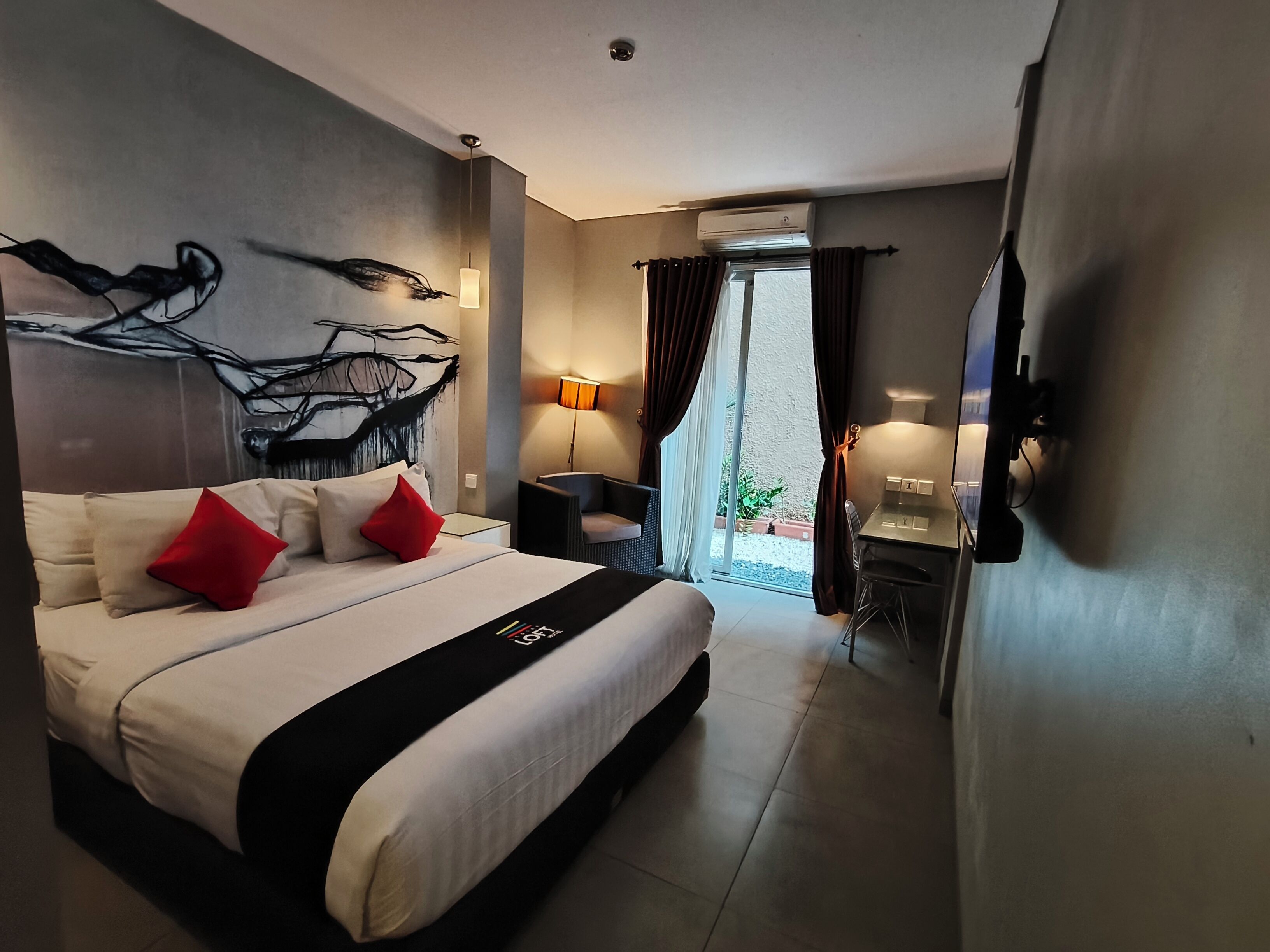 Habitación de hotel moderna con una cama grande, un escritorio, una silla, una lámpara y vistas al exterior.