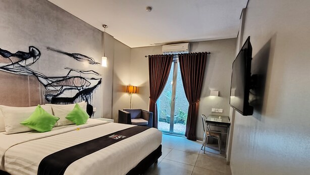 A modern hotel room with a large bed, a flat-screen TV, a desk with a chair, and a view of the outdoors through a sliding door. - Loft Legian Hotel (Legian)
