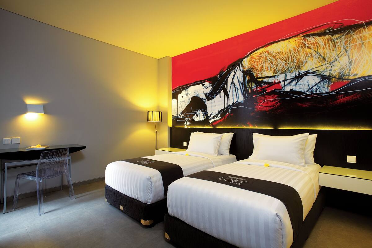 A hotel room with two beds, a desk, and a chair.