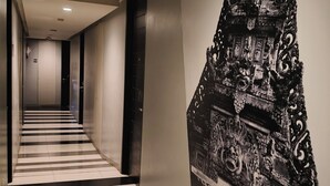 A hallway with a black and white checkered floor, a large black and white mural on the right, and a modern elevator on the left. - Loft Legian Hotel (Legian)