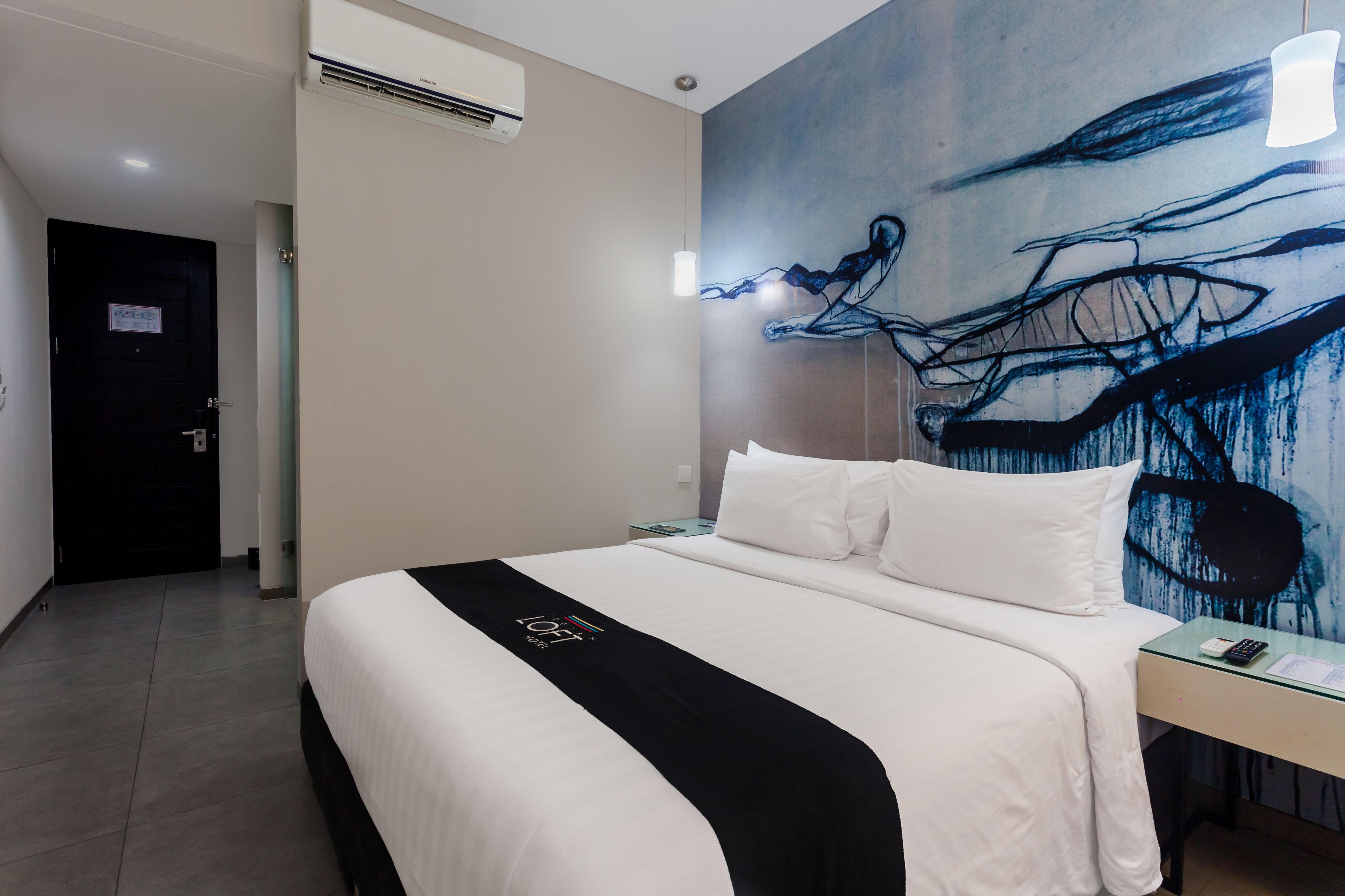 A hotel room with a large bed, a desk, and a wall with a blue abstract painting.