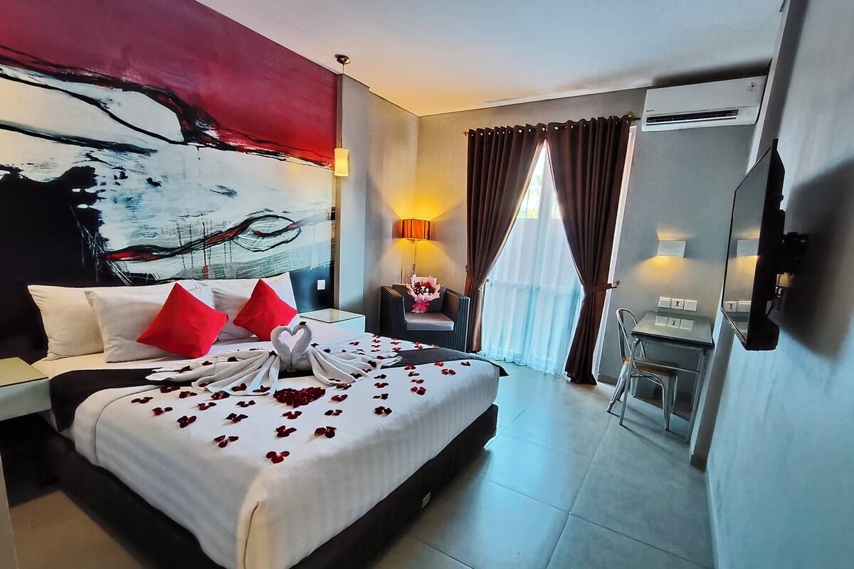 A hotel room with a bed, a desk, a chair, a lamp, and a painting on the wall.