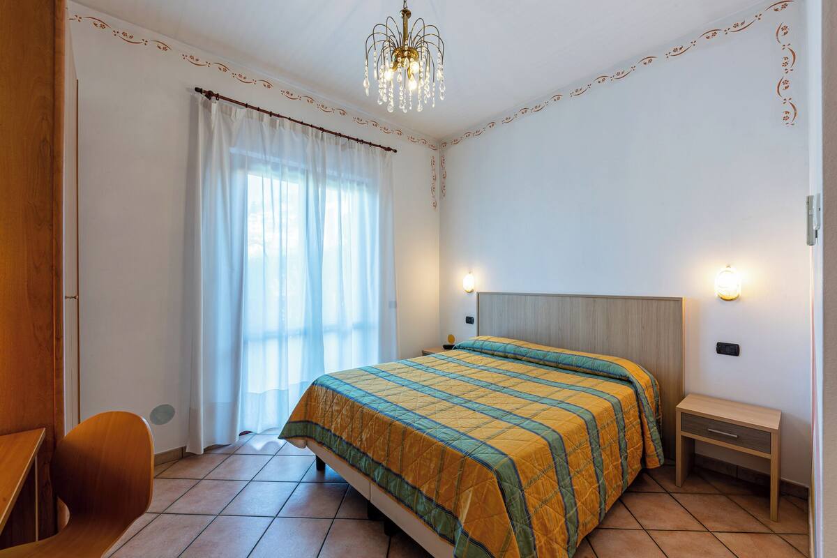 A bedroom with a bed, a bedside table, a chair, and a window with curtains.
