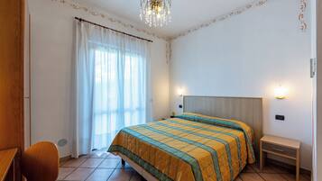 A bedroom with a bed, a bedside table, a chair, and a window with curtains.