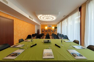Un salón de conferencias con una larga mesa, sillas, un proyector y una estantería al fondo.