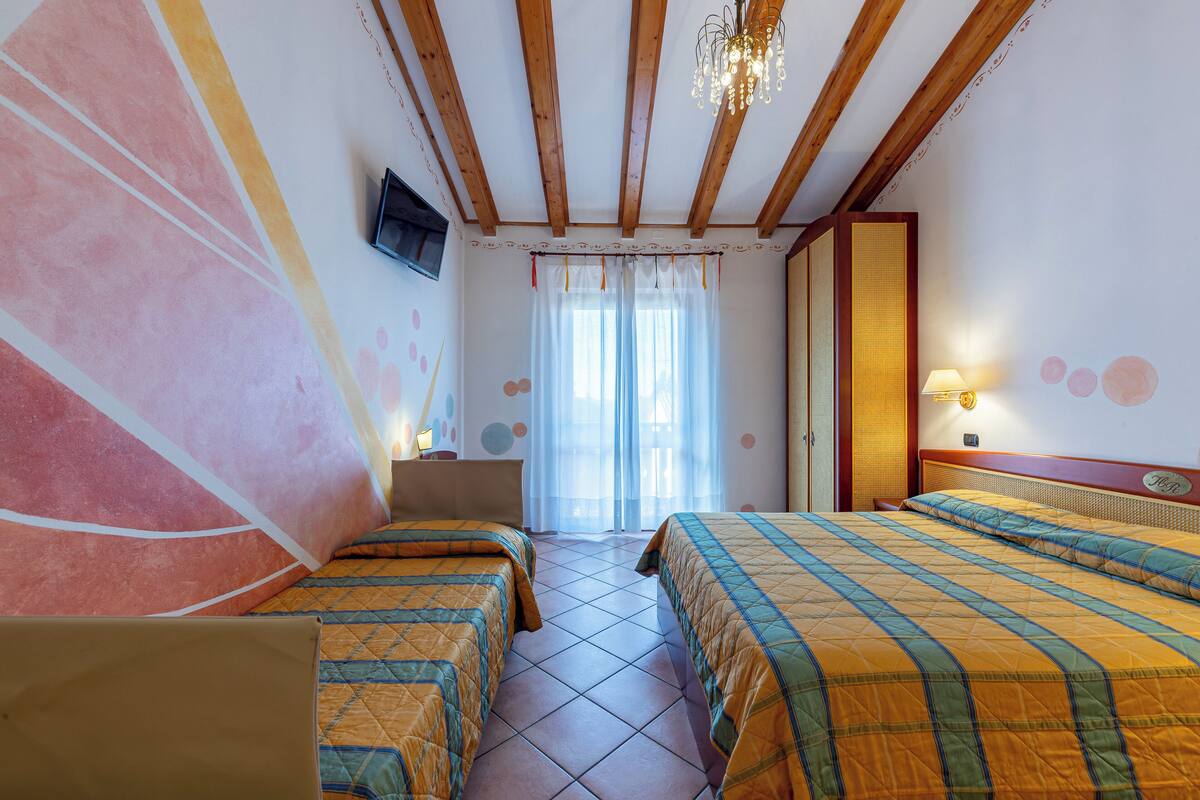 A hotel room with two beds, a television, a window with curtains, and a wooden ceiling.