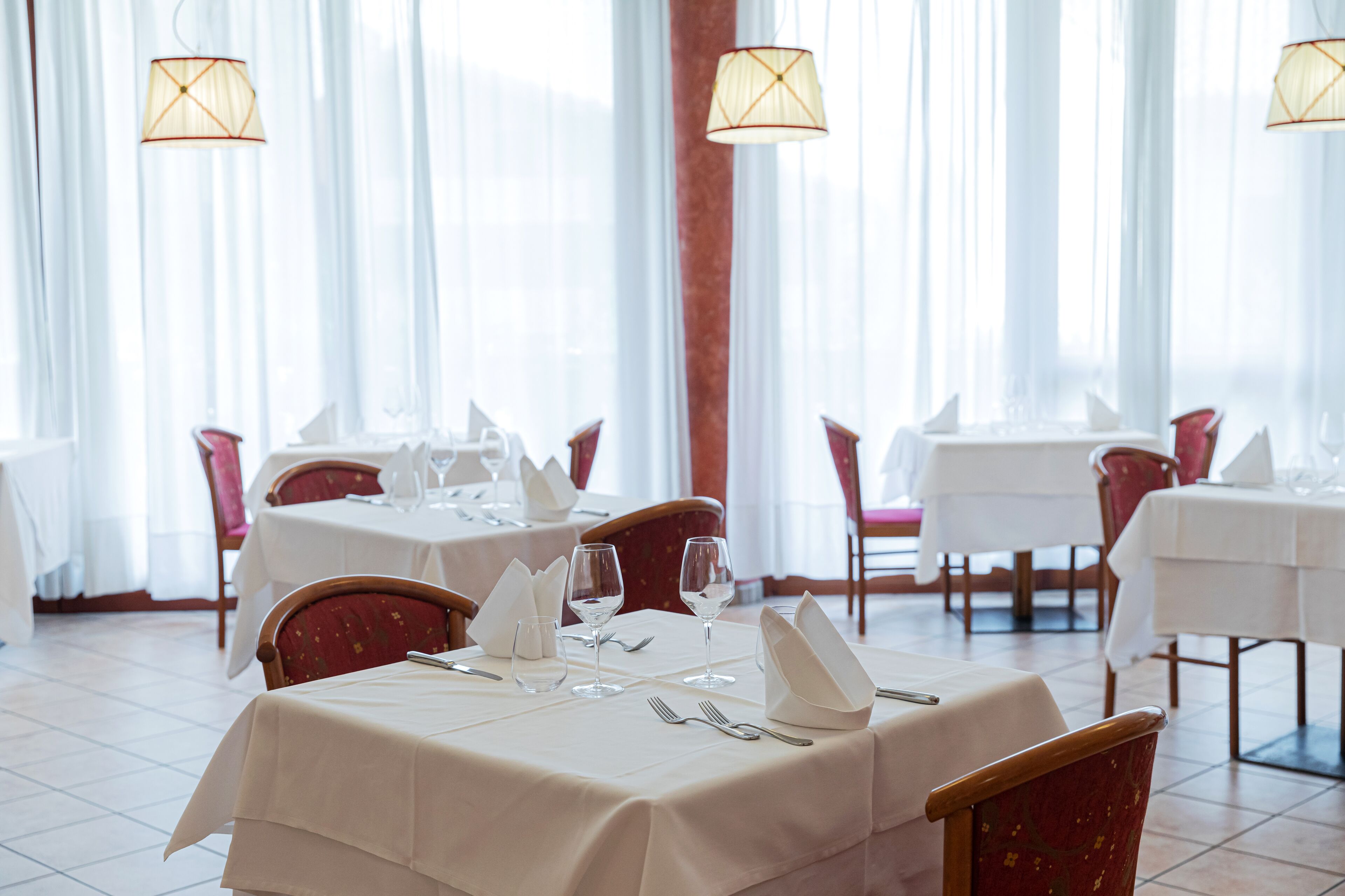 A restaurant with tables set for dining, chairs, and hanging lamps.