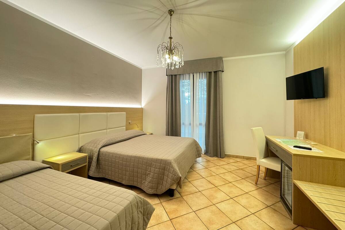 A hotel room with two beds, a desk, a TV, and a chandelier.