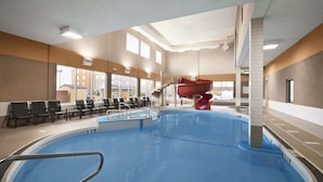 Ein Hallenbad mit roter Rutsche, Sitzbereich und Blick ins Freie.