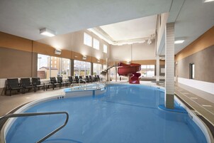 Una piscina interior con un tobogán rojo, zona de estar y vistas al exterior.