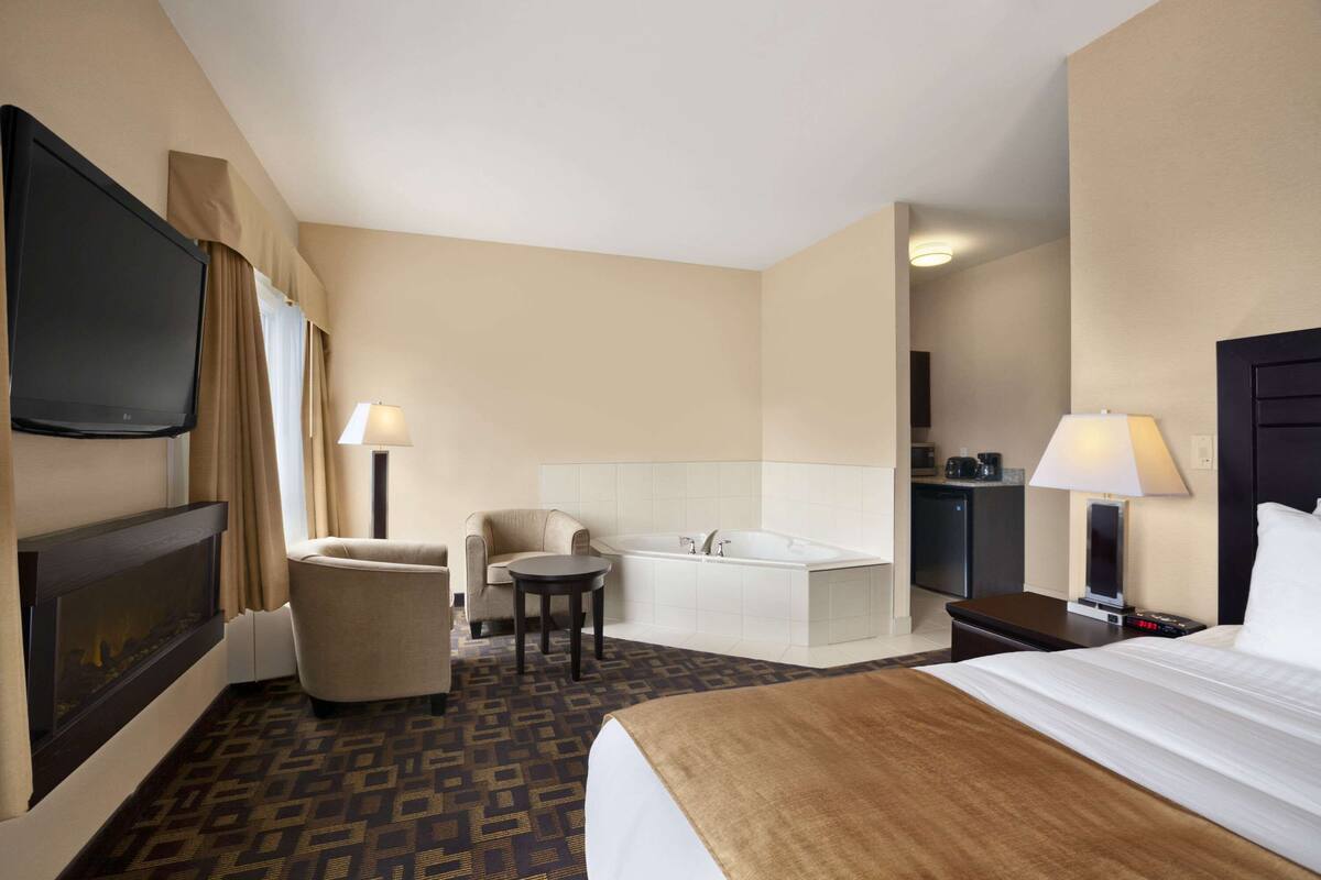Habitación de hotel con cama, televisor, sofá, mesita, bañera y escritorio con lámpara.